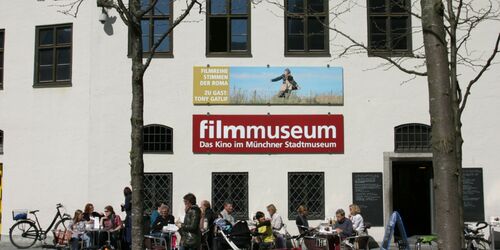 Filmmuseum München mit Menschen, die auf Terrasse davor sitzen