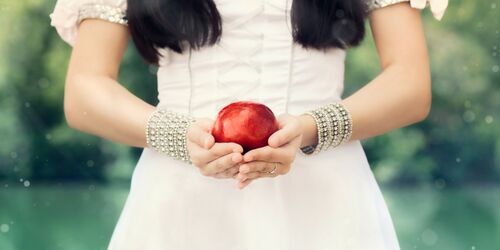Nahaufnahme einer Frau in weißem Kleid, die einen roten Apfel vor sich hält