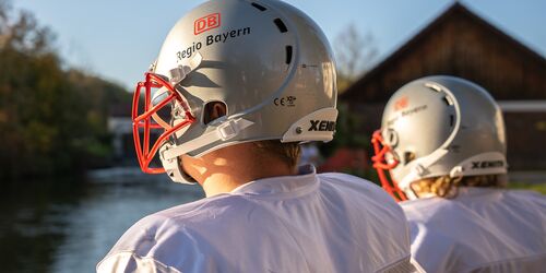 Zwei NFL Spieler mit Helmen mit DB Regio Logo