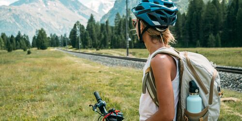 Radfahrerin neben Gleisen und vor Bergpanorama