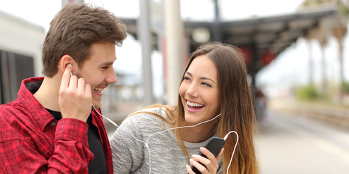 Junges Paar am Bahnsteig mit Handy und Kopfhörern