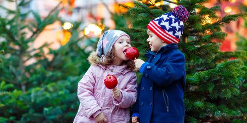 Zwei Kinder mit kandierten Äpfeln vor Weihnachtsbaum