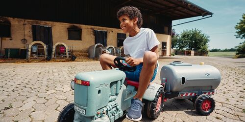 Kleiner Junge auf einem Kindertraktor auf dem Bauernhof