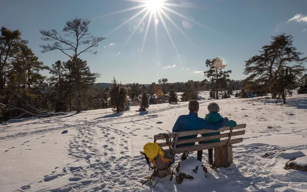 Verschneite Winterlandschaft mit einem Paar auf einer Sitzbank am Altmuehltal Panoramaweg