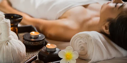 Frau auf Massagetisch mit Teelichtern und Handtüchern auf einem Tisch daneben