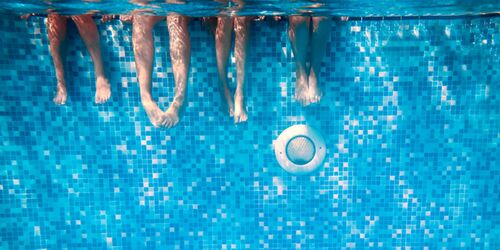 Sicht auf vier Paar Beine im Wasser vor einer Poolwand