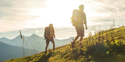 Paar, dass mit Sonne im Hintergrund einen Berg bewandert