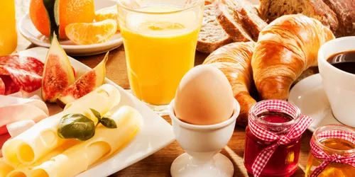 Gedeckter Frühstückstisch mit gekochtem Ei, Orangensaft, Käseplatte und Croissants