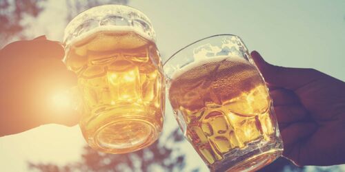 Gläserne Bierkrüge, die anstoßen mit Sonnenstrahlen Hintergrund