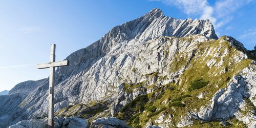 Gipfelkreuz am Osterfeldkopf mit Berg im Hintergrund