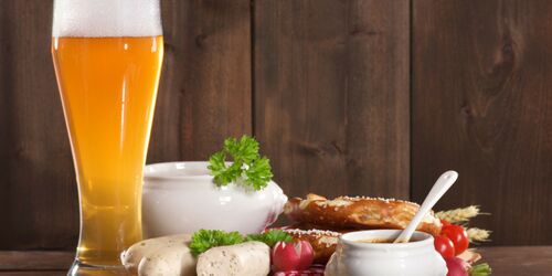 Holztisch mit Weißbier, Weißwurst, süßem Senf und Brezel