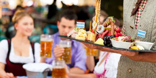 Paar in Tracht, das Bier trink mit Mann in Tracht, der Tablett trägt